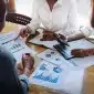 Grupo de profissionais analisando relatórios financeiros, gráficos e indicadores contábeis sobre uma mesa durante reunião de gestão empresarial.